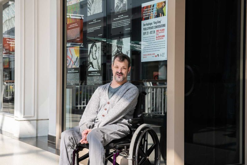 Dan Keplinger smiling and sitting in their wheelchair outside of Towson University.