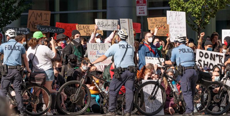 Police form a barrier with their bicycles to block off protestors who are holding signs in protest of George Floyd's murder.