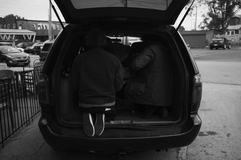 Bandmembers crouching in the backseat of their van, blending into the darkness. The white rubber soles of one of their shoes shine brightly.