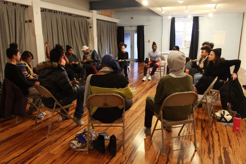 A group of people sitting in a circle on fold out chairs in a big room