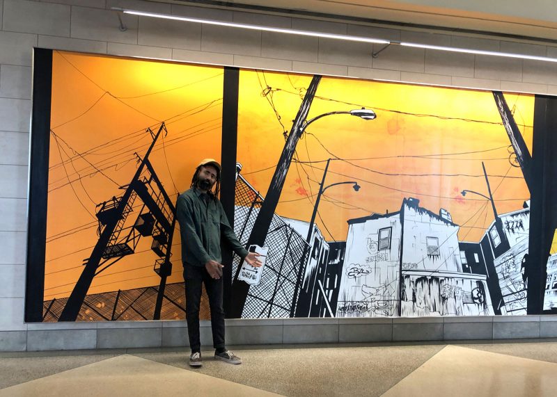 Derick Jones standing in front of their huge cityscape painting at the Philadelphia International Airport.