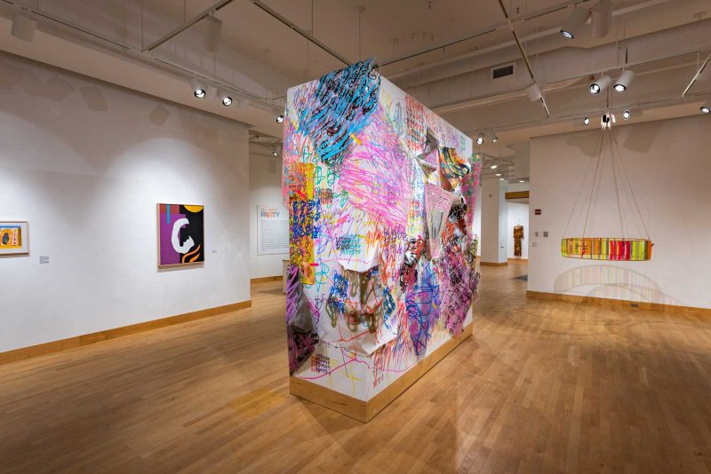 Installation view featuring a rectangular white panel in the center covered with Tim McFarlane paintings.