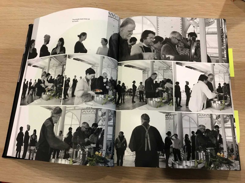 Olafur Eliasson's cookbook, open to a spread of photographs of he and his staff helping themselves to food from a buffet-style spread.