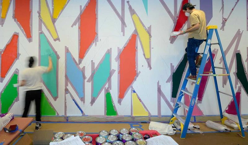 Two artists painting a brightly-colored geometric mural.