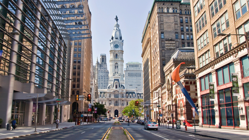 Philadelphia city hall captured from north broad street, with PAFA's paintbrush sculpture visible on the right amongst the tall city buildings.