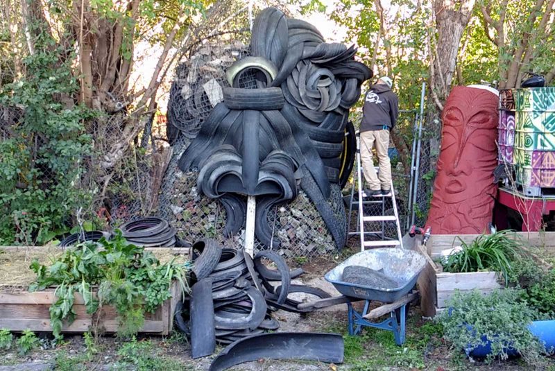 Velocity Fund grantee Pedro Ospina standing on a ladder, outdoors, working on a large sculpture resembling a creature, made out of tires.