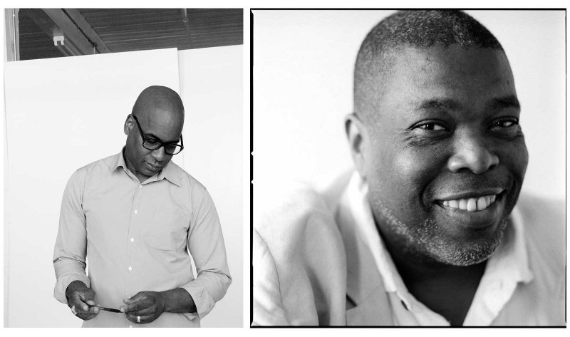 Glenn Ligon wearing black framed glasses and a button up shirt, standing and looking downwards while holding a pen. Hilton Als wearing a suit jacket and shirt and looking sideways at the camera with a big grin.