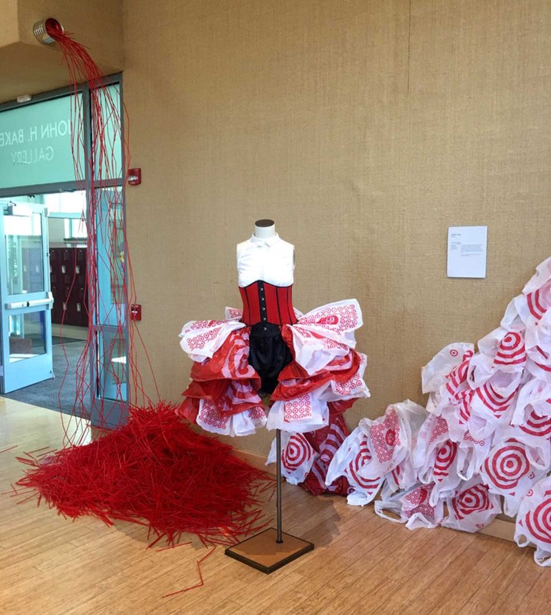 A carnival inspired hybrid dress, made out of a button-up shirt, a corset, and target bags functioning as a tutu, displayed on a mannequin inside of a building. 