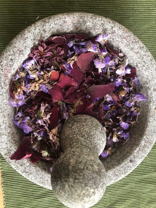A rock mortar and pestle with purple and pink dried flowers ground up inside of it.