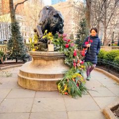 Imani Roach smiling and carrying two flowers past a sculpture and floral arrangement in Rittenhouse Square Park, Philadelphia.