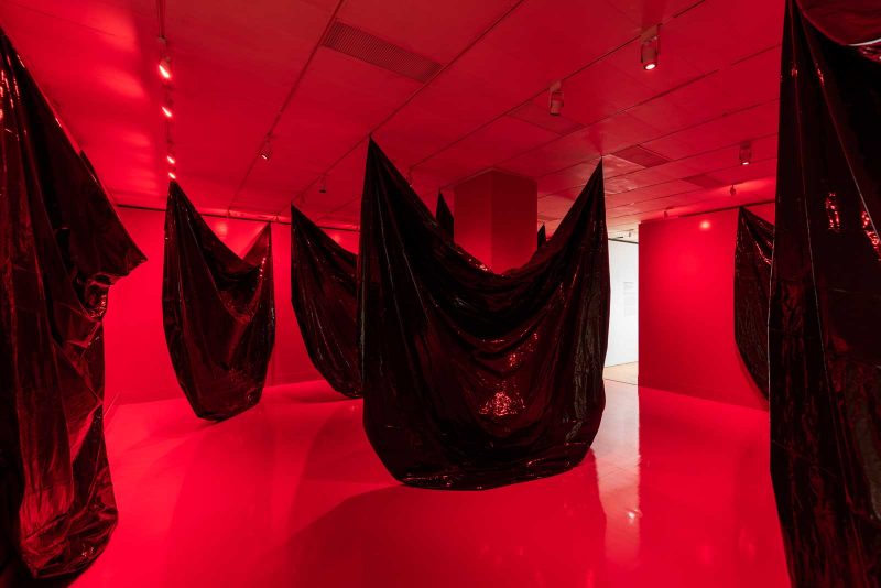 Artwork by Senga Nengudi at the Philadelphia Museum of Art. A large room filled with red light and giant black plastic sheets hung so that they slouch downwards in the middle.