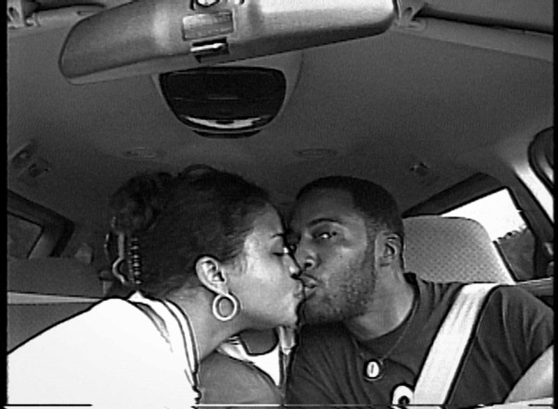 Fox and Rob Rich kissing in the front seat and front passenger seat of a car.