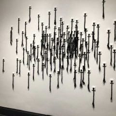 Large wall installation of black fabric braided to resemble Black woman hair that is hung in random clusters on the wall.