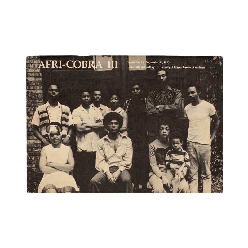 Group photo of 10 Black women and men, and 1 child, posing together with serious expressions, in front of a building.