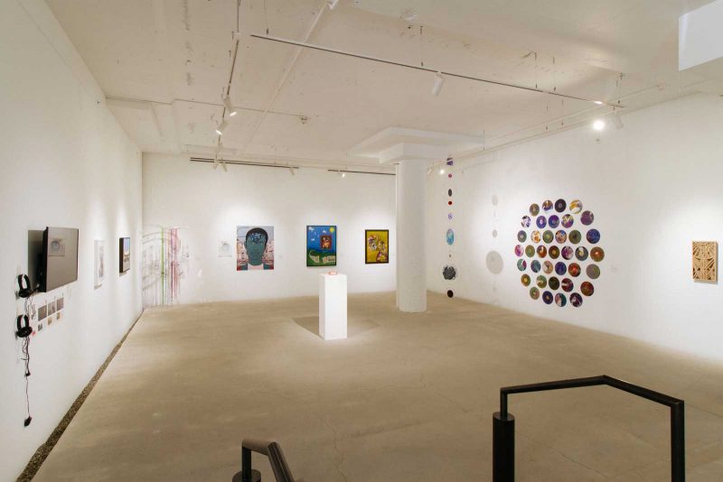 Installation view of group art exhibition 'Unfolding,' featuring framed paintings and hanging installations. 