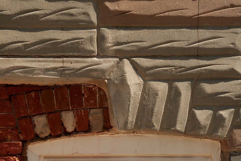 Close-up view of Formstone on a building, where a section is not covered and shows the original red brick.