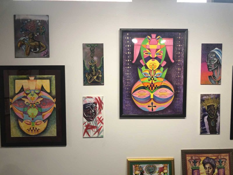 Gallery wall featuring multiple artworks ranging from fantastical portraits of Black bodies mixed with mythological imagery; and abstract geometric shapes personified.