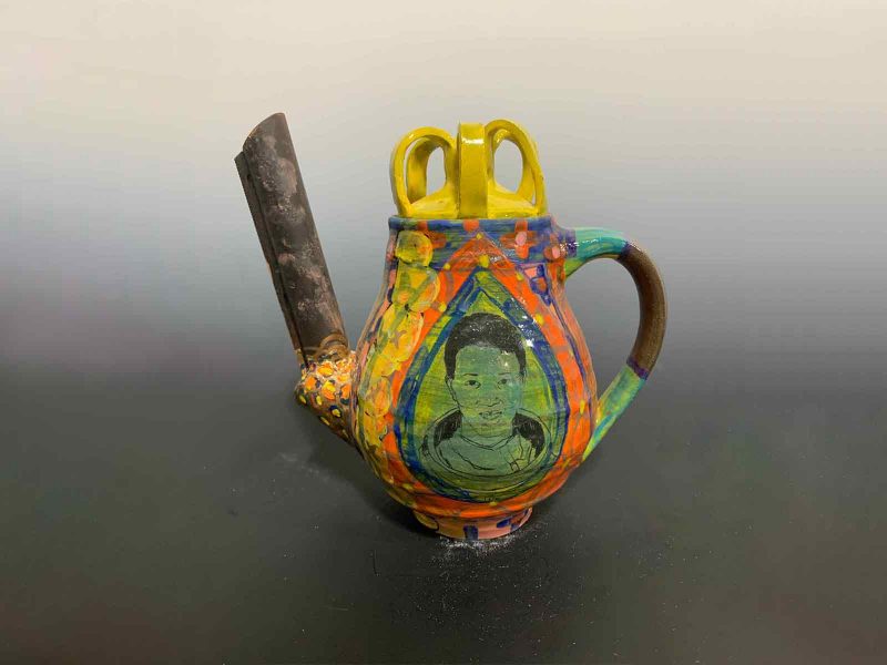 Colorful ceramic teapot with exaggerated spout and handle, with a portrait of Mae Jemison drawn in the center of the body of the pot.