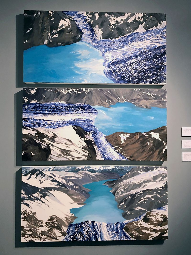 Three rectangular paintings of a glacier from different perspectives, hung vertically on top of one another.