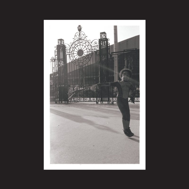 A photograph shows a young Black boy in front of a tall wrought iron fence.