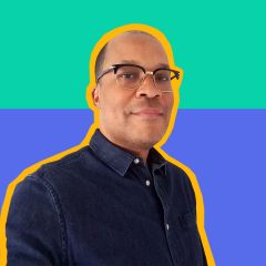 Rah Crawford, a Black man with a buzz cut, wearing 50's style browline glasses and a dark blue denim button up, and smiling into the camera, superimposed onto a colorful digital background.