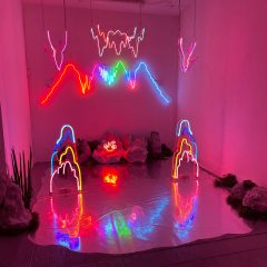 Installation of neon glass sculptures, faux rocks, and a real plant on a silver fabric platform; the installation resembles an electric cavern.