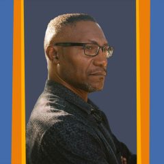 Headshot of Eric Battle, a Black man with a high fade wearing black square framed glasses and a black button up shirt, with a serious expression.