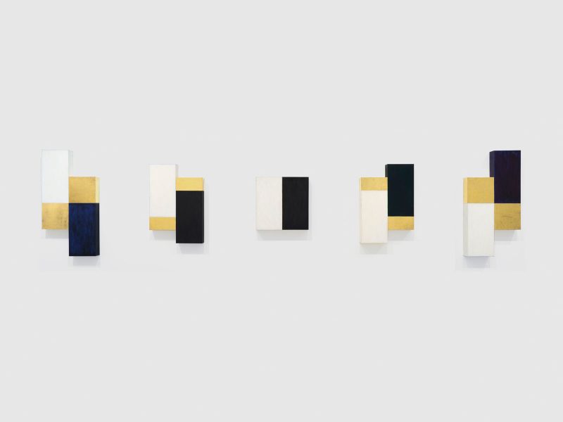 Series of 5 abstract paintings painted white, almost black, and gold; two conjoined rectangular panels seem to shift into place (left), make a square (center) and then out of place again (right).