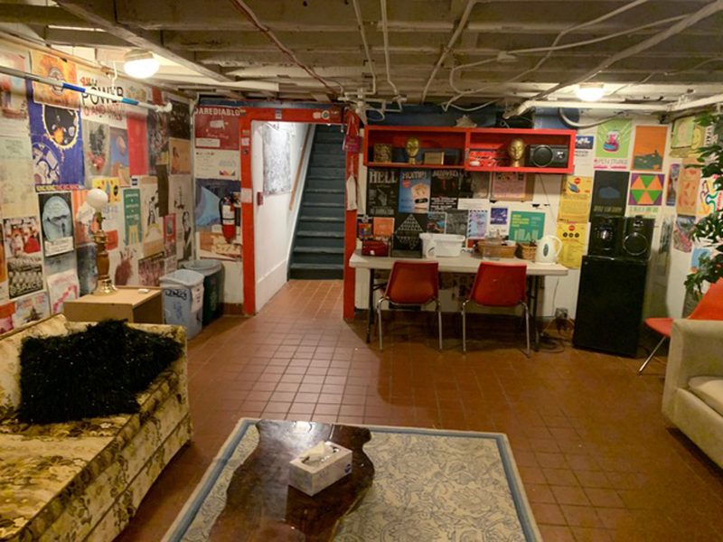 Work space in SPACE, with walls plastered with flyers and other posters, a desk with two chairs, and two couches facing each other and a coffee table in between. 