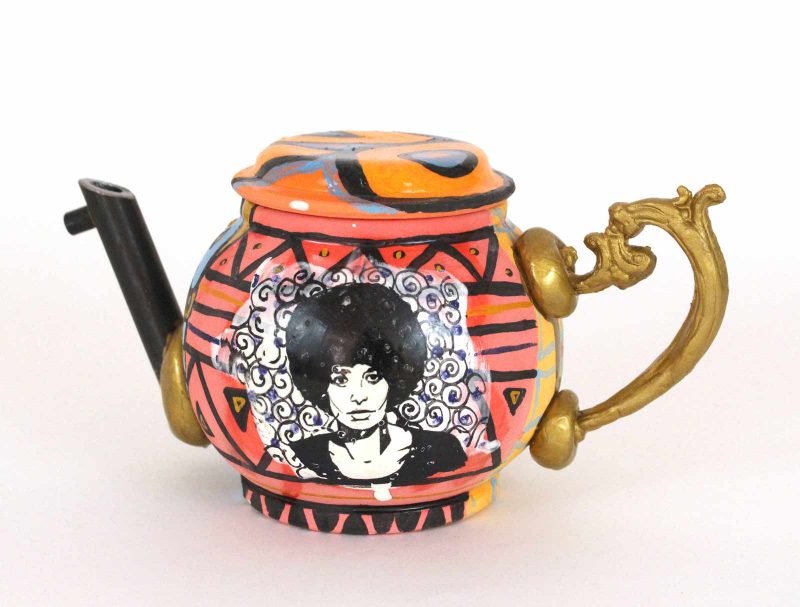 Black and white portrait of Angela Davis painted onto the center of a ceramic teapot with an ornate gold handle and a spout fashioned out of a gun barrel.