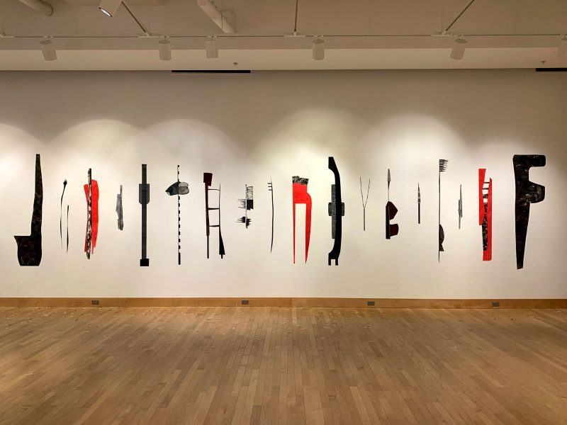 White wall with many thin and tall illustrations arranged side by side on the wall, taking up the majority of the wall, red and black abstracted images of hair tools