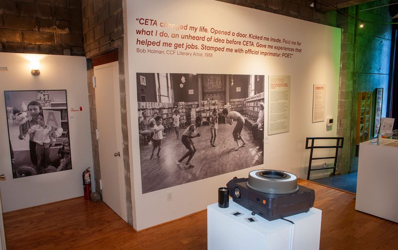 Gallery exhibition with black and white photos of people, and text documentation of the impact of the Comprehensive Employment and Training Act (CETA). 