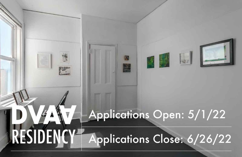 White text announcing DVAA's open call for residency applications through 6/26/22, overlaid on a photograph of Da Vinci Art Alliance's gallery space, featuring small black & white and green paintings hanging on the wall nearby a folding chair and table facing a window.