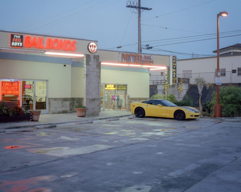 A photo of a the end of a small strip mall, with two lighted signs visible and fancy yellow car parked out front.