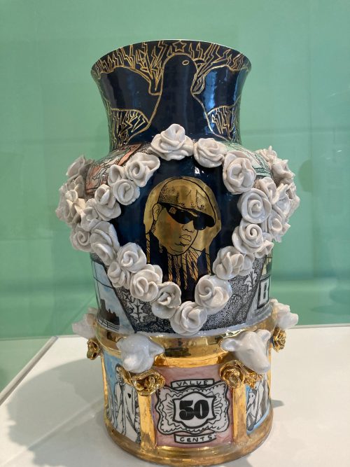 An intricately patterned vase by Roberto Lugo depicts the Notorious B.I.G. Surrounding the central image there are smaller illustrations and sculpted flowers.