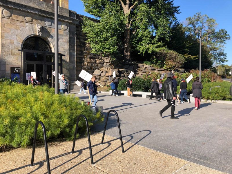 Striking workers circle the area outside the north entrance of the Philadelphia Museum of art holding picket signs.