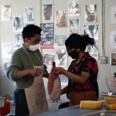 Two people are looking at an unfinished ceramics piece together in an art studio.