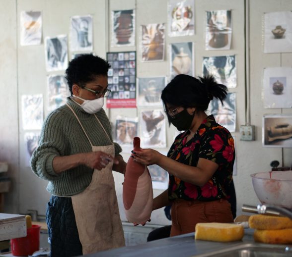 Two people are looking at an unfinished ceramics piece together in an art studio.