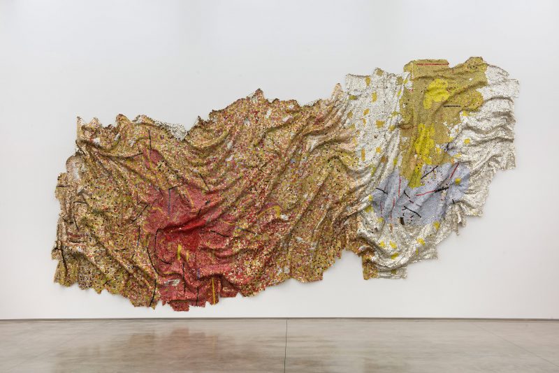 A sculptural wall hanging by El Anatsui uses recycled materials to create a textile-like surface.