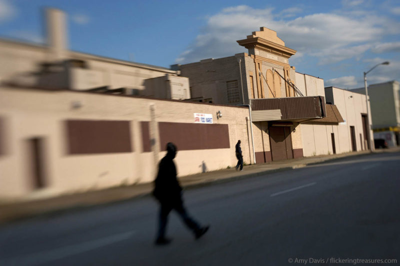 In this photo by Amy Davis, two silhouetted figures walk down the block in front of a large beige building.