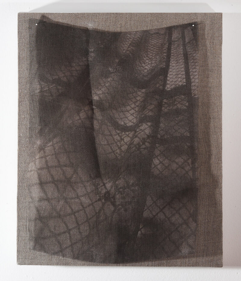 A monochrome abstract artwork on translucent cloth pinned to a board covered with brown linen, shows an overall pattern of a netting, whose squares grow larger at the bottom while at the top they are minuscule, while the translucent cloth seems to have many folds and wrinkles in it that create strong asymmetrical counter pattern to the strong netting pattern.