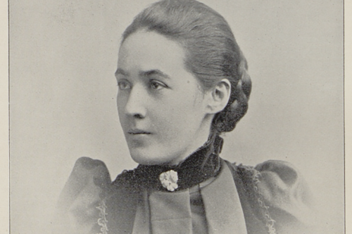 A white woman with her hair in a braided bun is pictured from the shoulders up. The photo is old and her clothing reflects the 19th century. Her gaze is focused toward the left side of the camera.