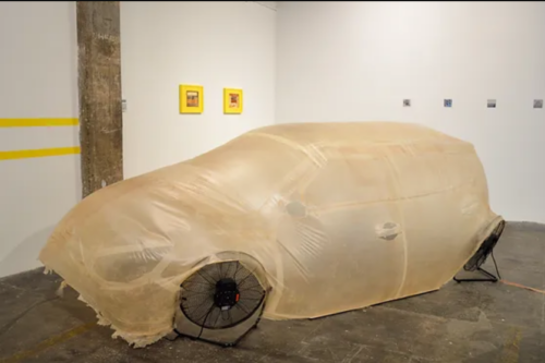 A plastic bag like material with a yellow tinge is filled by four fans creating the shape and impression of a car. Each of the fans acts as a wheel. 