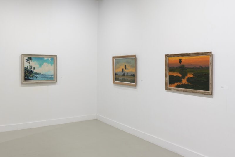 Art gallery walls show a corner of the gallery with three framed landscape paintings hung at eye level, showing Florida’s rich flora and colorful skies, painted by three painters of the Highway Men collective of Southern Florida.