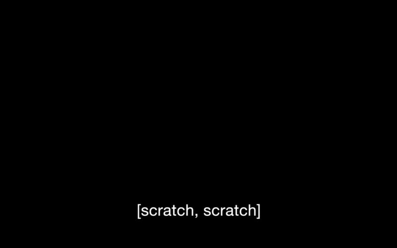A pitch black rectangle, which is taken from a video by Carolyn Lazard, holds white text on the bottom that says, “[scratch, scratch].”