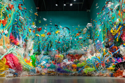 A glorious symphony of color from recycled plastics creates a plastic reef filled with aquatic life in a turquoise painted gallery space.