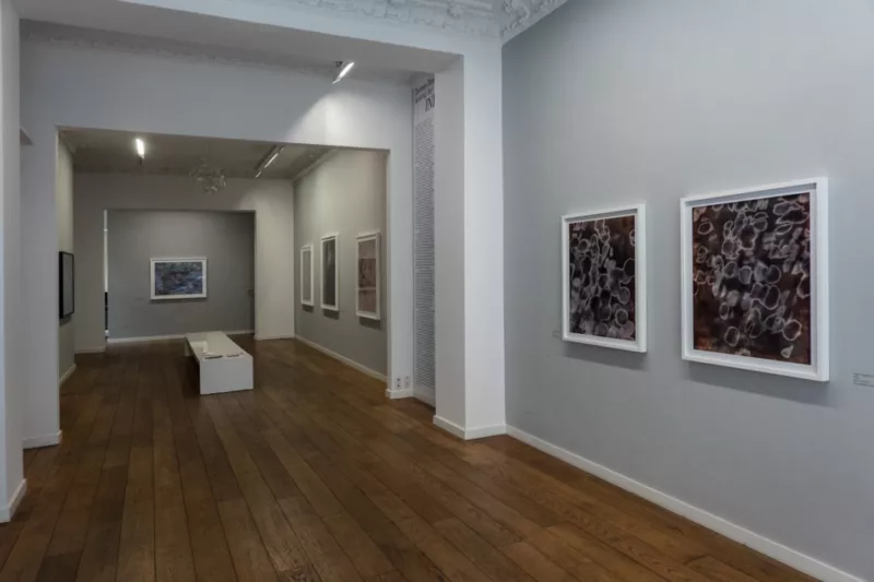 An image of a gallery space with dark wood floors and grey walls displying the work of Thomas Brummett's exhibition "Seeking the Infinite".