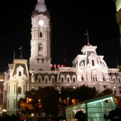 A color photo from 2004 shows a dramatic, night-time view of Philadelphia City Hall, brightly lit by special flood lights.