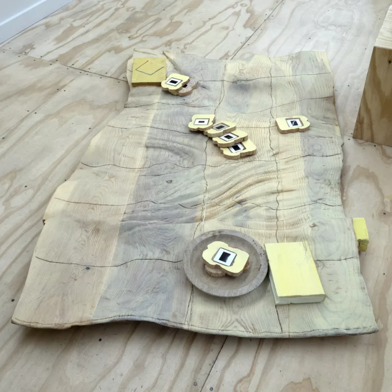 a slab of wood sculpted into the shape of a picnic cloth, pieces of wood bread scatter the cloth, while others are on plates. Each slice of bread holds a slide of American History vacations.