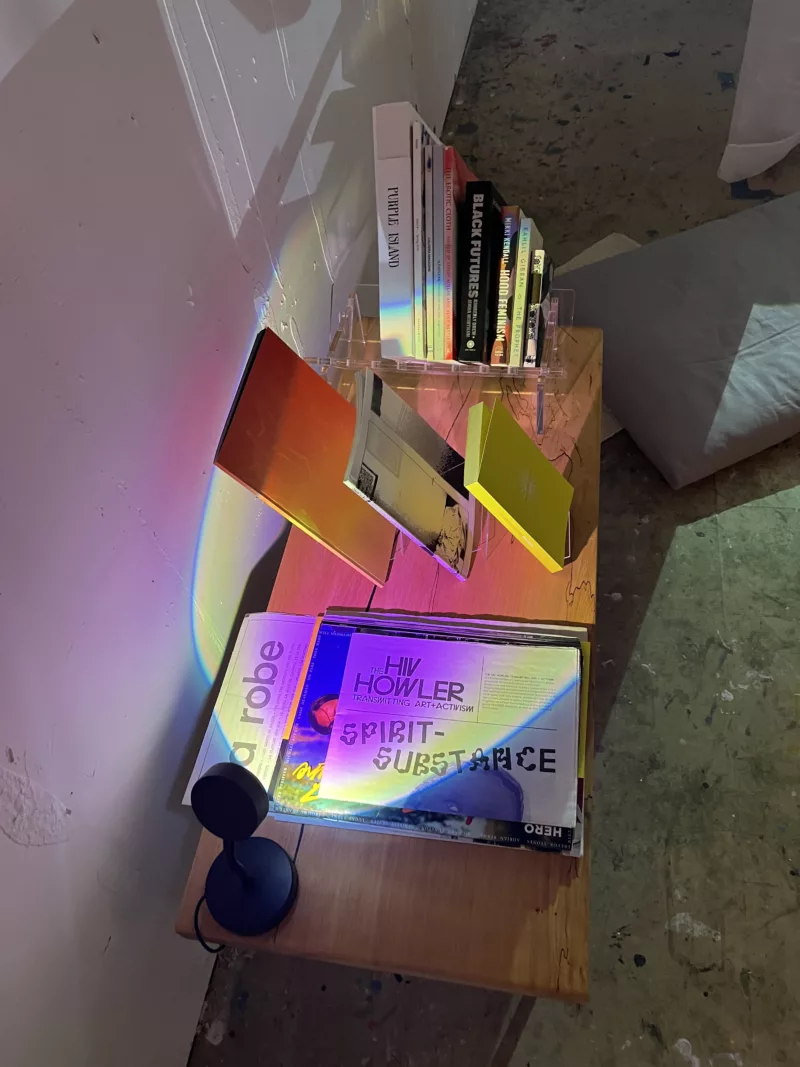 a wood table of reading materials with a sunset lamp casting its colorful hues on the book covers.